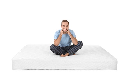 Young man sitting on mattress against white background