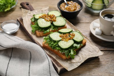 Photo of Tasty cucumber sandwiches with arugula, mustard and coffee on wooden table