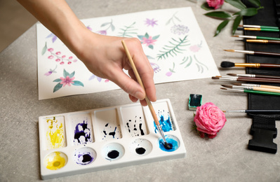 Photo of Woman painting flowers with watercolor at grey stone table, closeup