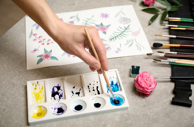 Woman painting flowers with watercolor at grey stone table, closeup