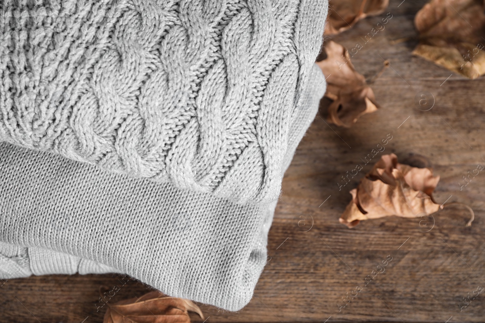 Image of Stack of folded warm sweaters and dry leaves on wooden table, above view