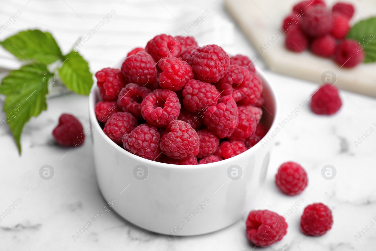 Photo of Bowl with fresh ripe raspberries on white marble table, closeup