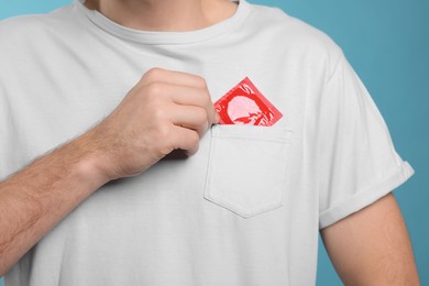Photo of Man putting condom in his pocket on light blue background, closeup