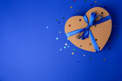 Beautiful heart shaped gift box with bow and confetti on blue background, top view. Space for text