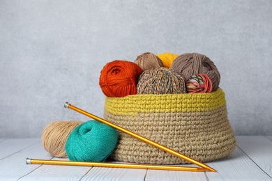 Photo of Soft woolen yarns and knitting needles on white wooden table