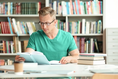 Photo of Young man reading book at table in library