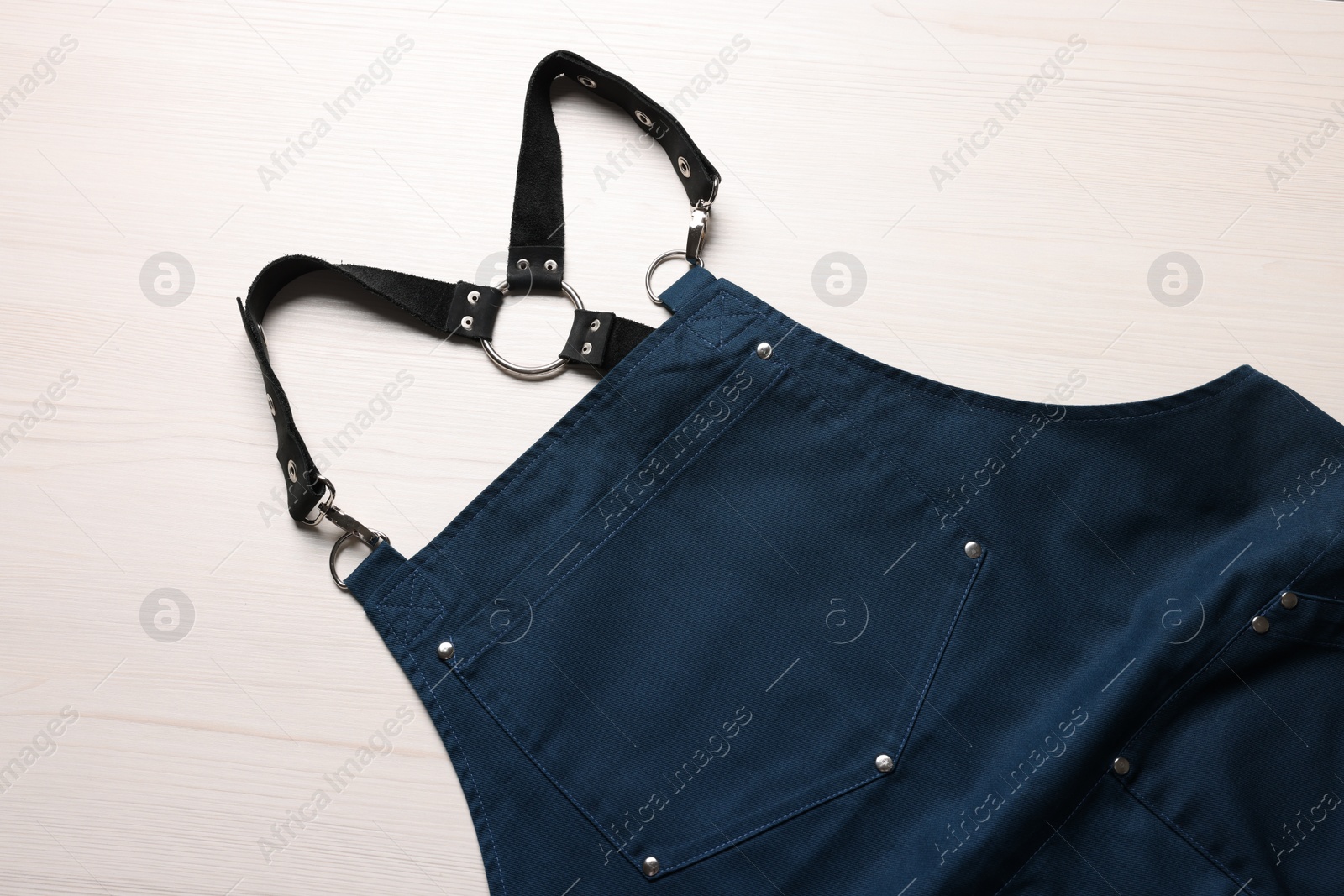 Photo of Stylish dark blue apron on white wooden table, top view. Mockup for design