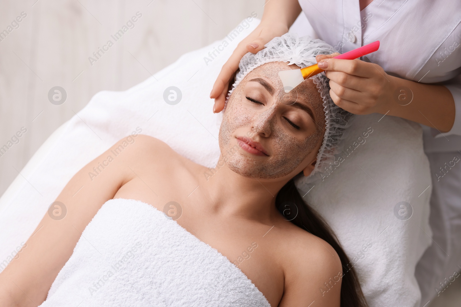 Photo of Cosmetologist applying mask on woman's face in clinic, top view