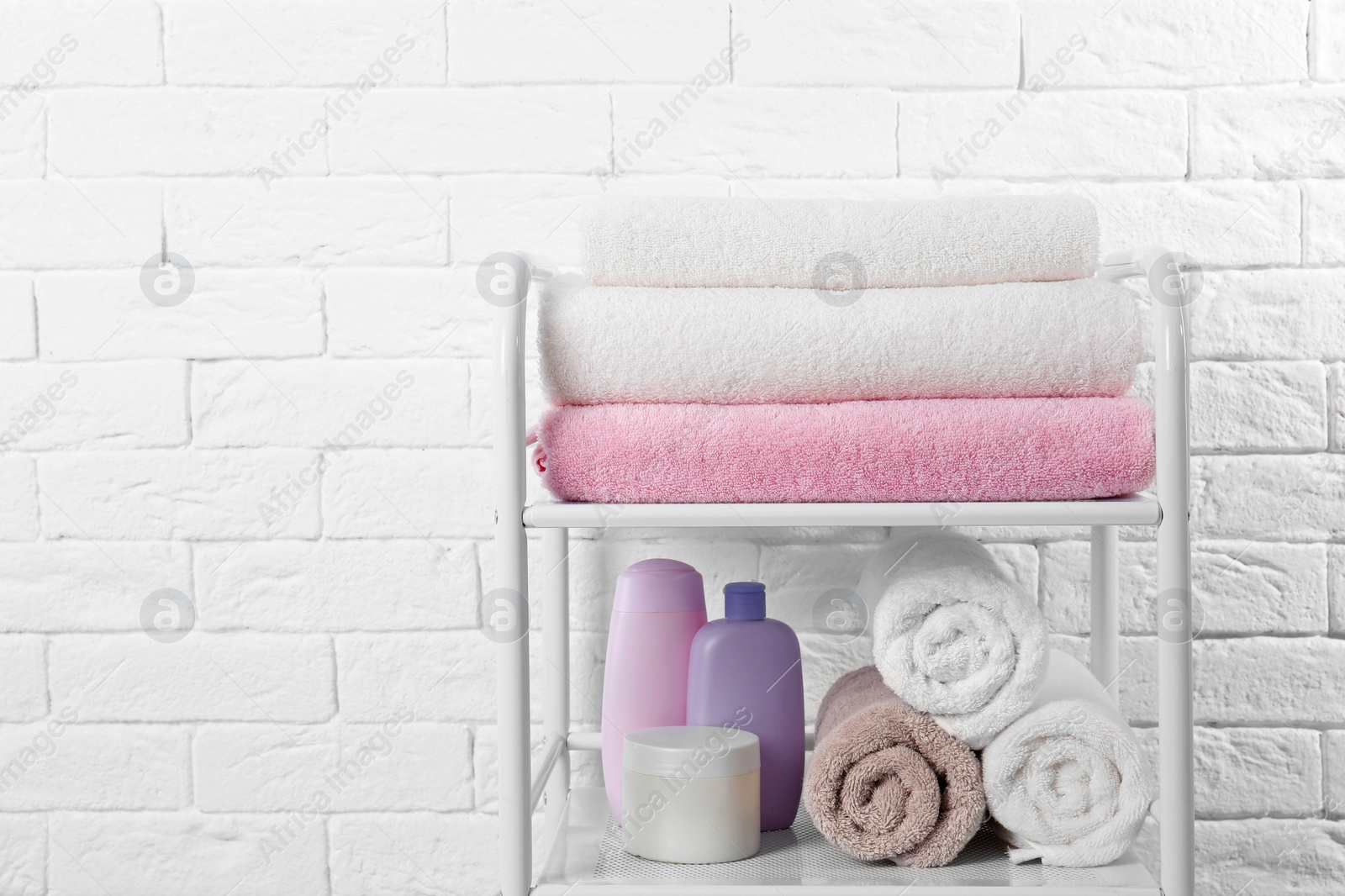 Photo of Shelving unit with clean towels and toiletries near brick wall. Space for text