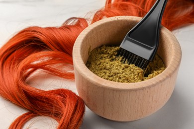 Photo of Henna powder, brush and red strand on white table, closeup. Natural hair coloring