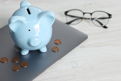 Photo of Piggy bank, coins, glasses and laptop on white table. Space for text