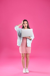 Full length portrait of shocked young woman in casual outfit with laptop on color background