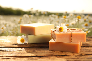 Photo of Chamomile soap bars on wooden table in field