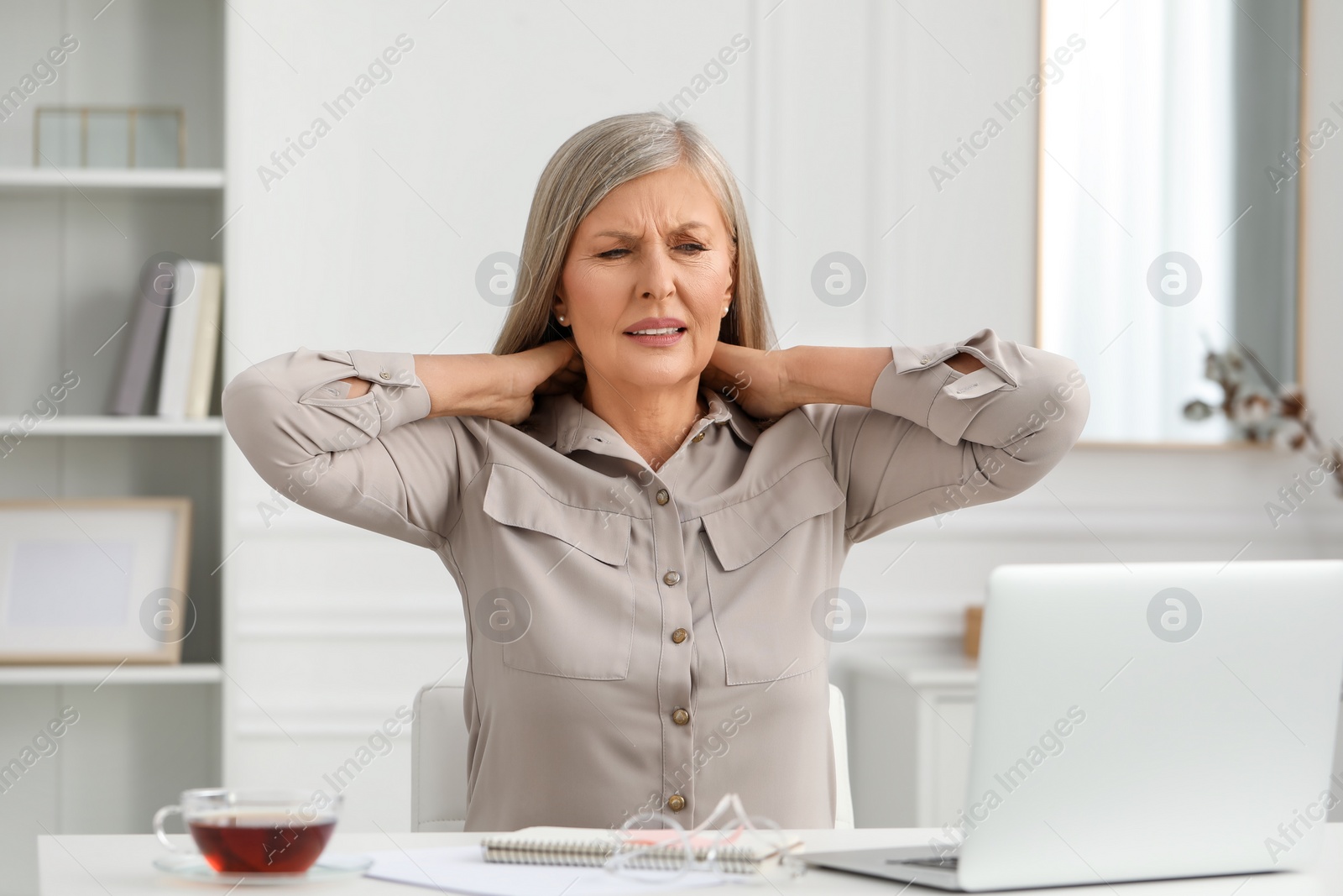 Photo of Woman suffering from neck pain at workplace in room