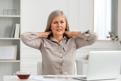 Woman suffering from neck pain at workplace in room