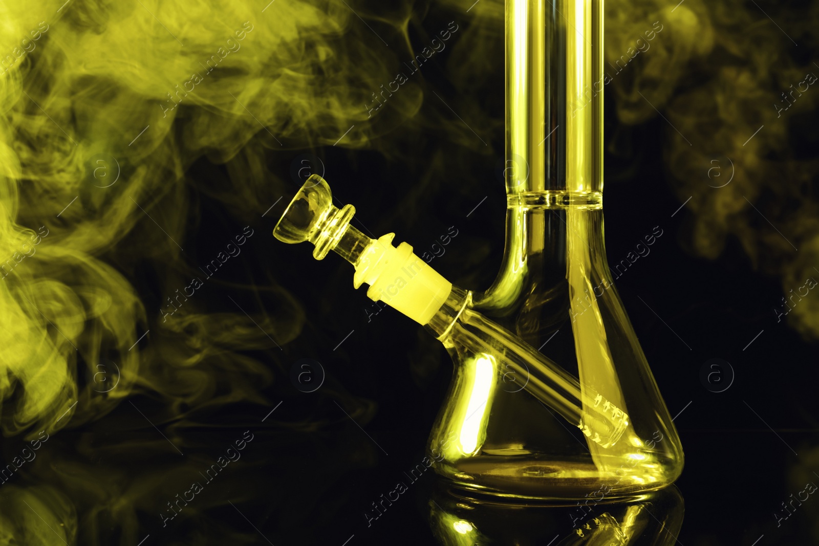 Photo of Closeup view of glass bong with smoke on black background, toned in yellow. Smoking device