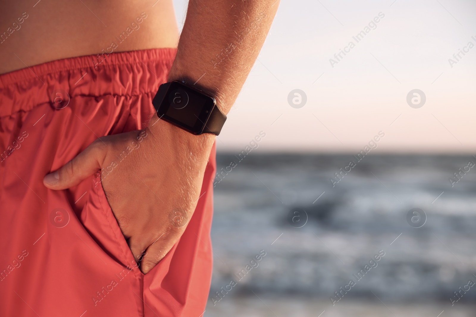 Photo of Man wearing smart watch on beach at sunset, closeup