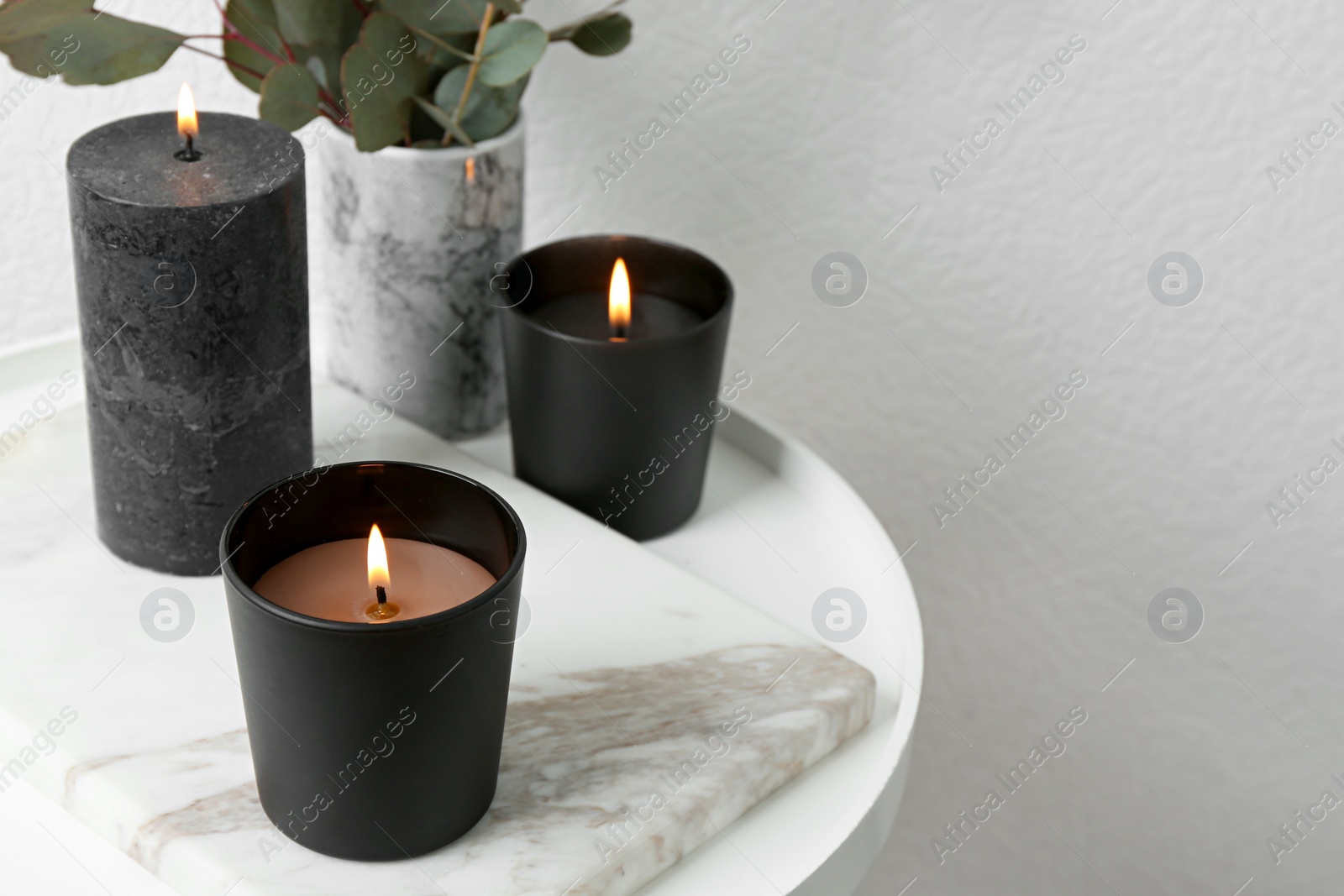 Photo of Burning candles and green branches on table at white wall, space for text