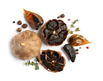 Photo of Aged black garlic with thyme and peppercorns on white background, view from above