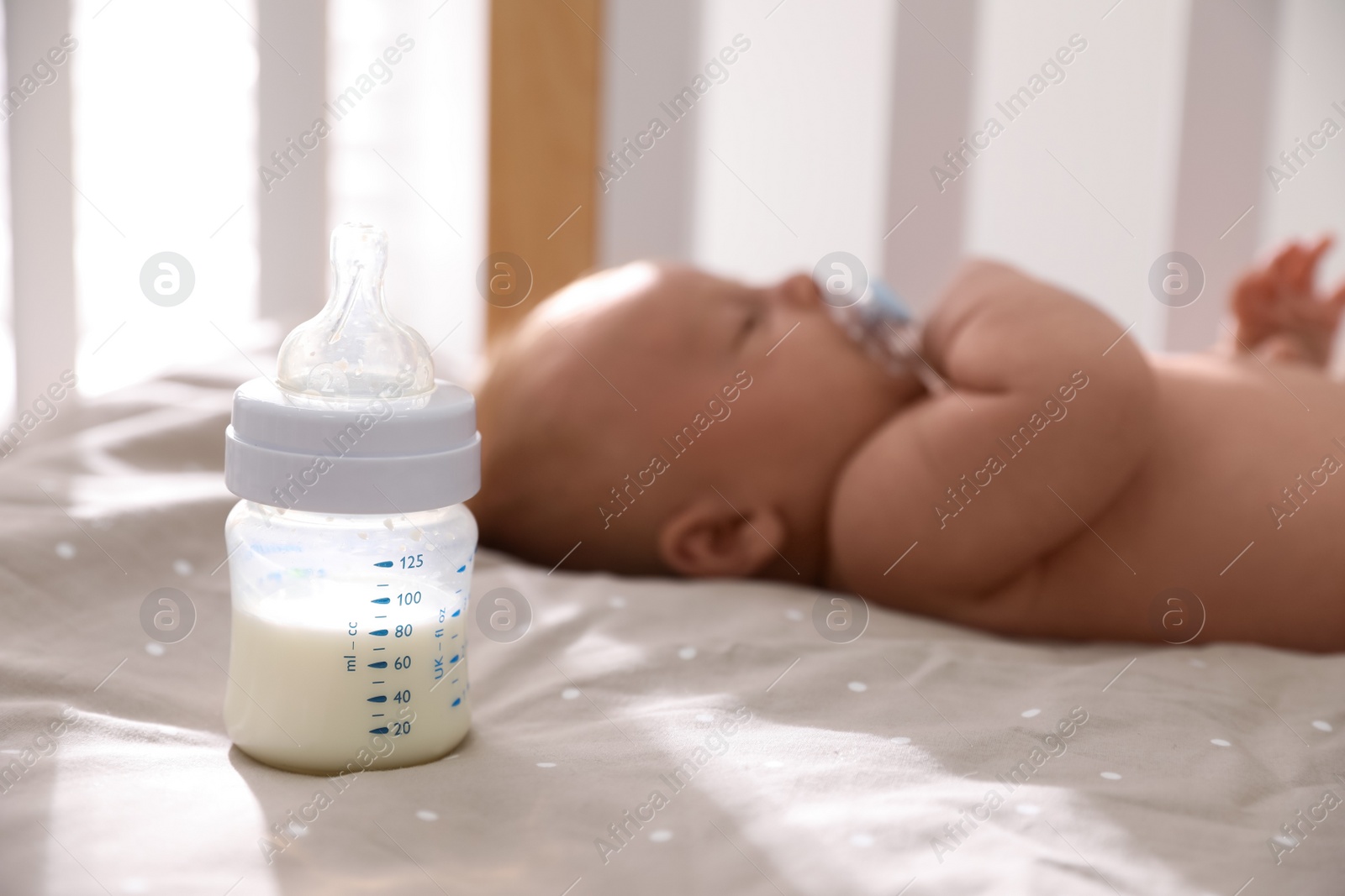 Photo of Healthy baby sleeping in cot, focus on bottle with milk