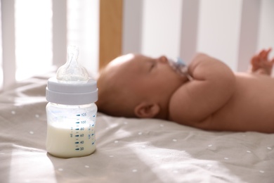 Photo of Healthy baby sleeping in cot, focus on bottle with milk
