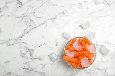 Photo of Bowl of frozen carrot and ice cubes on marble table, flat lay composition with space for text. Keeping vegetables fresh