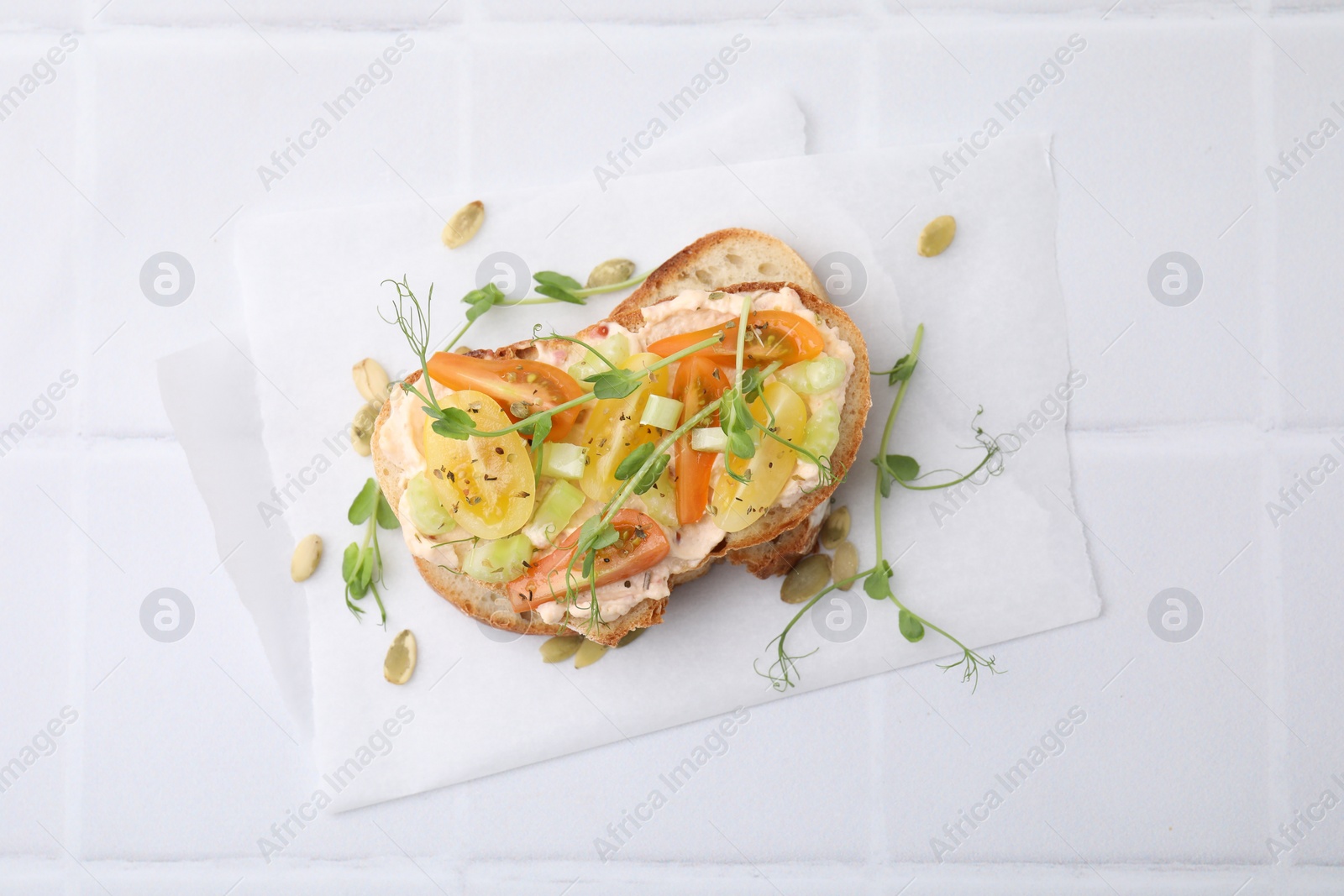 Photo of Tasty vegan sandwich with tomatoes, celery and microgreens on white tiled table, top view