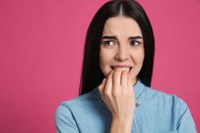 Photo of Young woman biting her nails on pink background