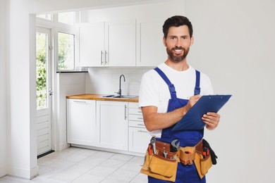 Plumber with clipboard and tool belt in kitchen, space for text