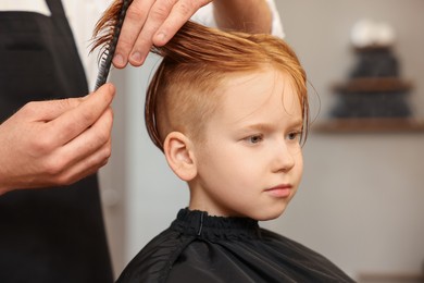 Photo of Professional hairdresser combing boy's hair in beauty salon, closeup