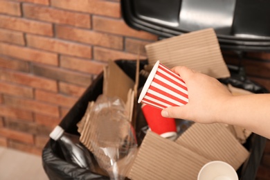 Photo of Young woman throwing popcorn cup in trash bin indoors, closeup. Waste recycling
