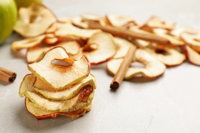 Delicious apple chips and cinnamon on light grey table, closeup. Space for text