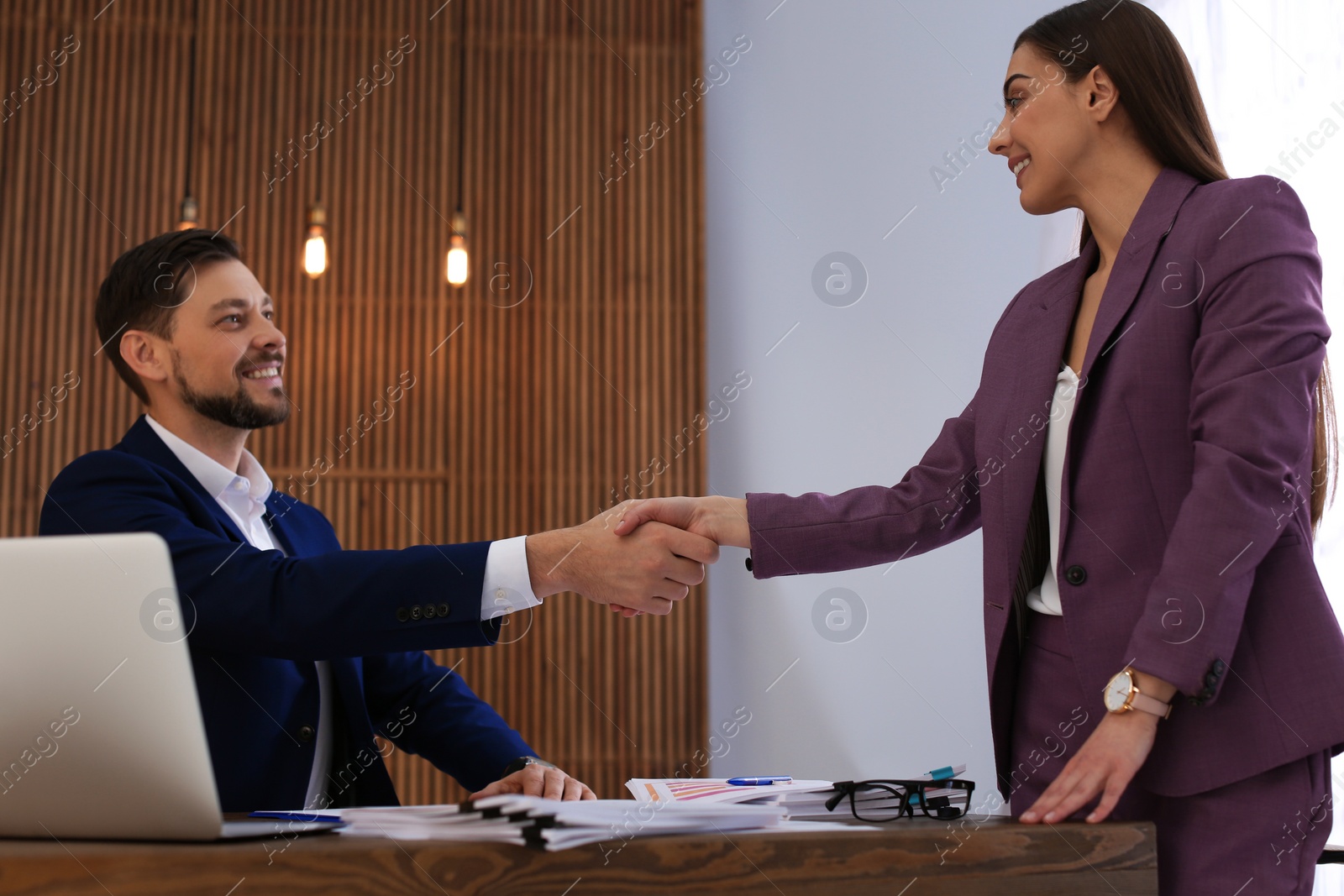 Photo of Office employees shaking hands over table with documents at workplace