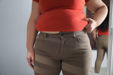 Photo of Overweight woman in tight shirt and trousers at home, closeup
