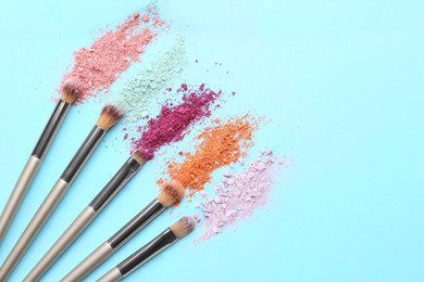 Photo of Makeup brushes and scattered eye shadows on light blue background, flat lay. Space for text