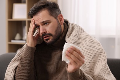 Photo of Sick man with tissue wrapped in blanket on sofa at home. Cold symptoms