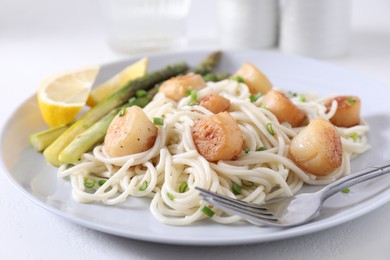 Delicious scallop pasta with asparagus, green onion and lemon served on white table, closeup