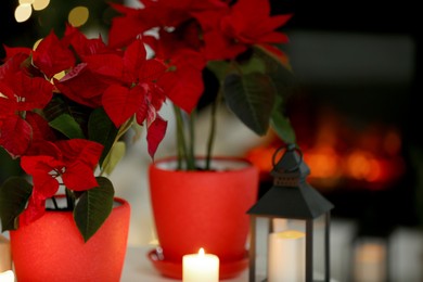 Photo of Potted poinsettias, burning candles and festive decor in room, closeup with space for text. Christmas traditional flower