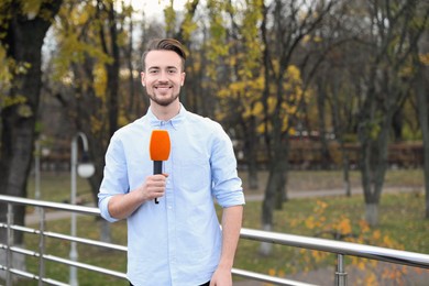 Photo of Young male journalist with microphone working in park
