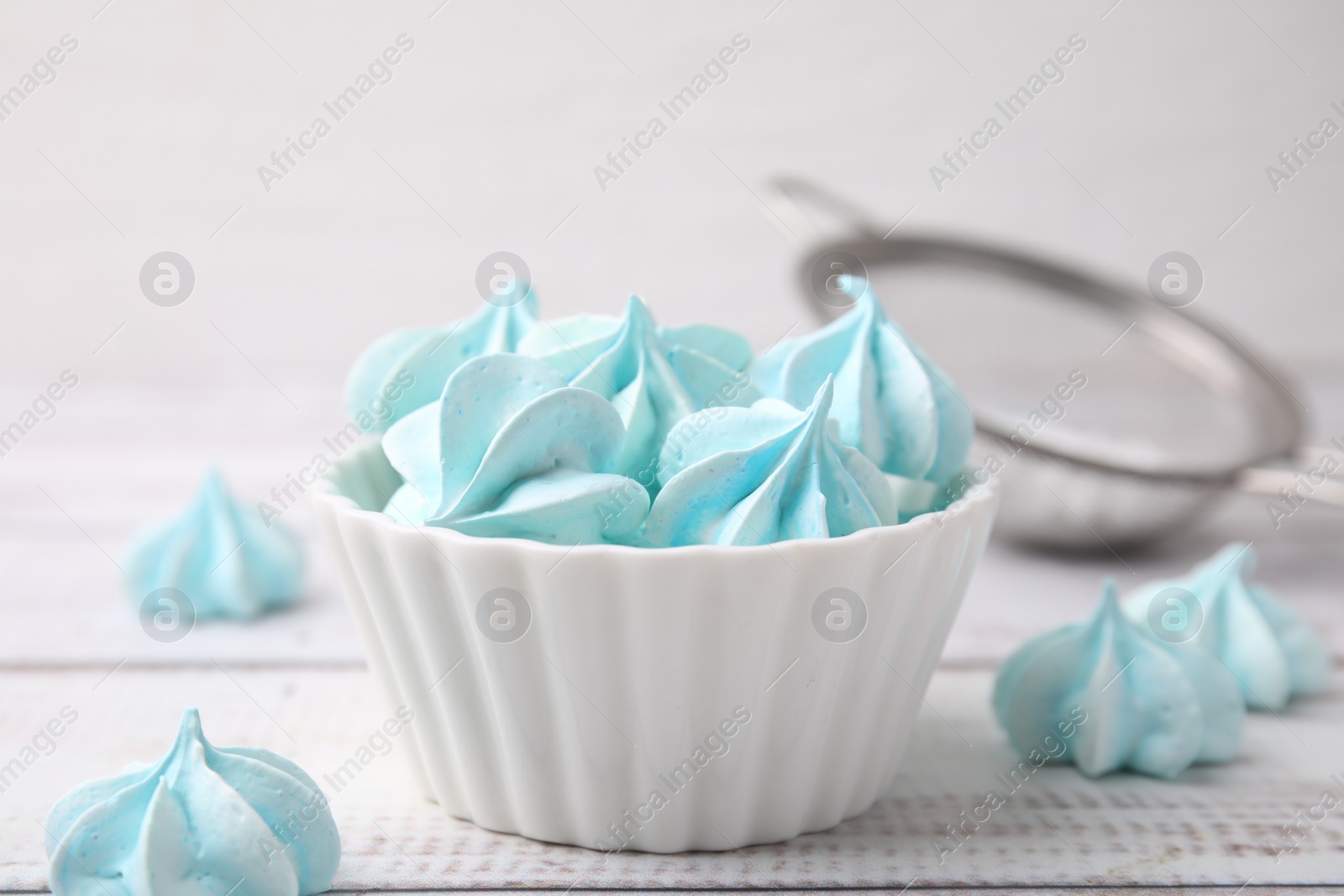 Photo of Tasty meringue cookies in bowl on white wooden table