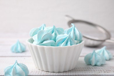 Tasty meringue cookies in bowl on white wooden table