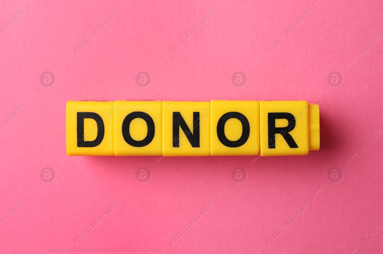 Photo of Word Donor made of yellow cubes on pink background, flat lay