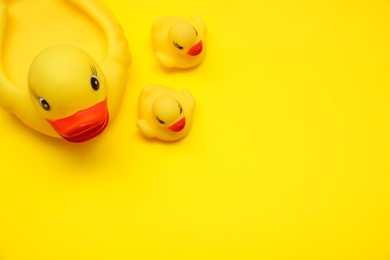 Rubber toy ducks on yellow background, flat lay. Space for text