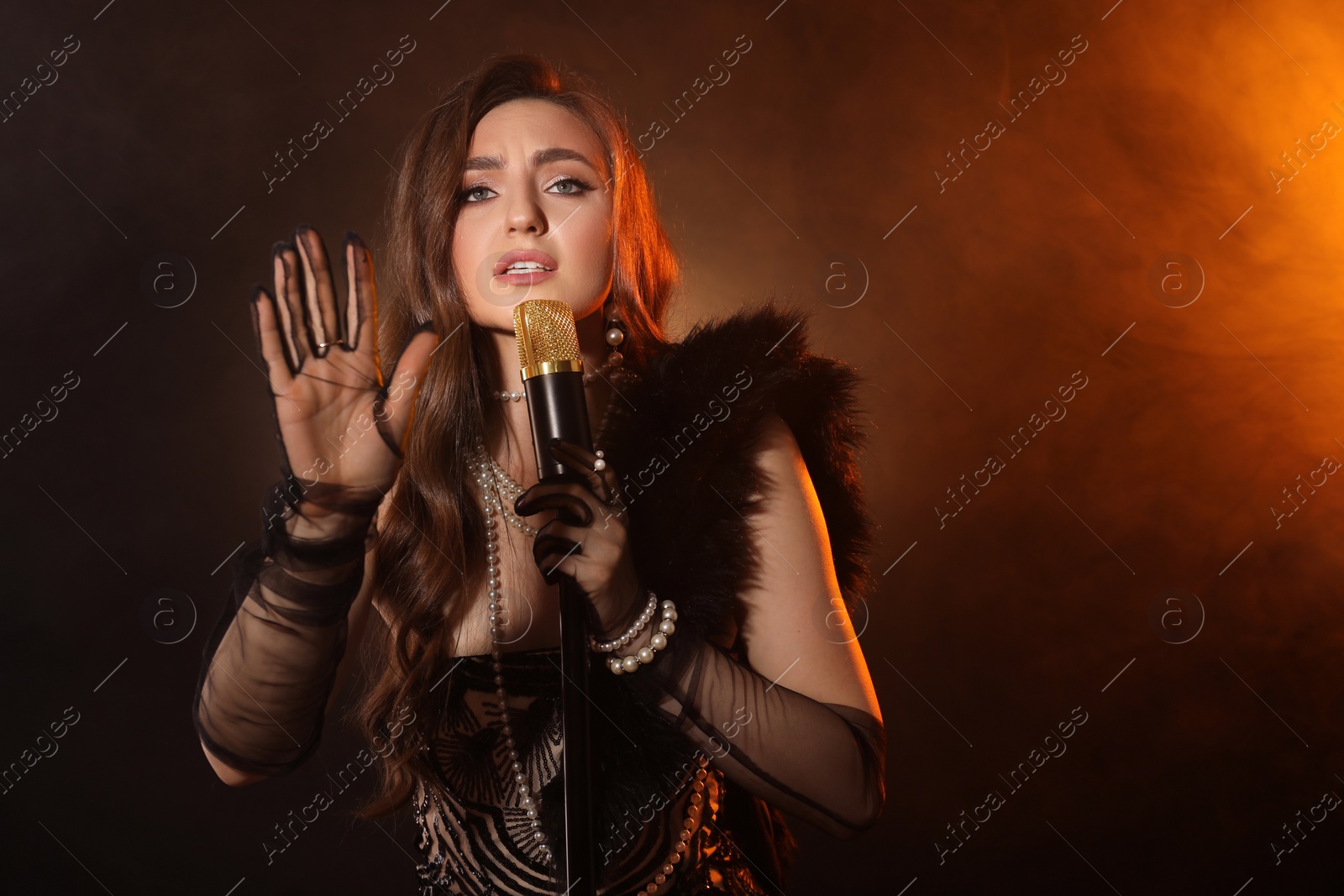 Photo of Beautiful young woman with microphone singing in color lights and smoke