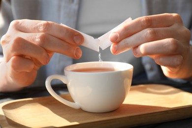 Woman adding sugar into cup of tea at table, closeup