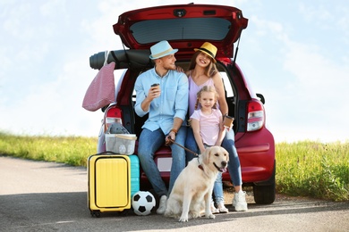 Photo of Young family with luggage and dog near car trunk outdoors