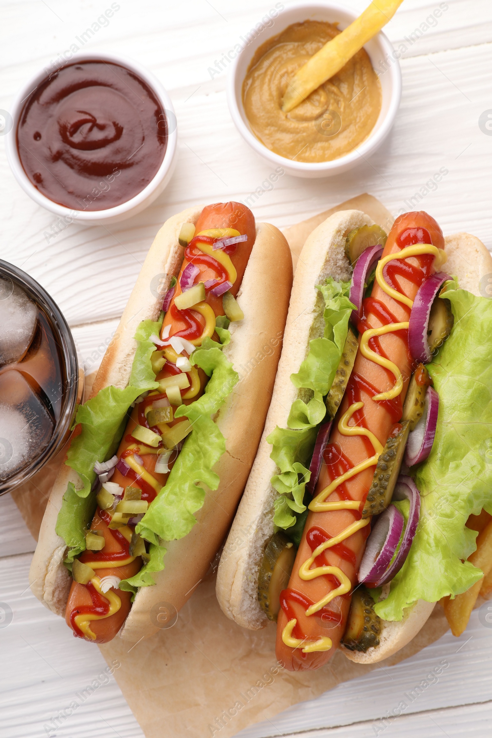 Photo of Delicious hot dogs with lettuce, onion and pickle served on white wooden table, flat lay