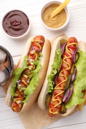 Delicious hot dogs with lettuce, onion and pickle served on white wooden table, flat lay