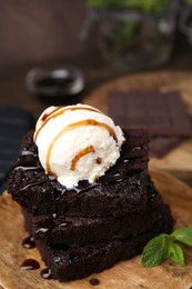 Photo of Delicious brownies served with ice cream and caramel sauce on table, closeup
