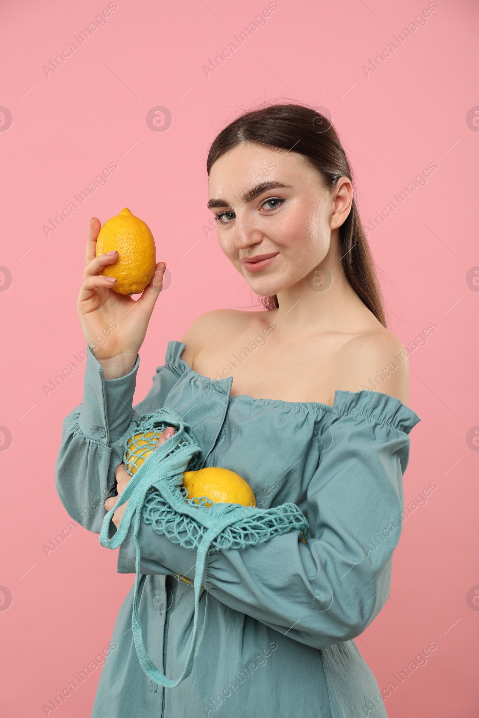 Photo of Woman with string bag of fresh lemons on pink background